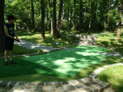 Ein Minigolfplatz in einem grünen Wald. Ein Kind spielt mit einem Schläger auf der Bahn.