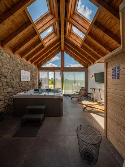 Ein modernes Zimmer mit Holzdecke und großen Fenstern. Im Raum befinden sich ein Whirlpool und ein gemütlicher Sessel.