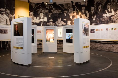 Een tentoonstelling met meerdere witte displays die historische beelden presenteren. Op de achtergrond zijn historische foto's aan de muur te zien.