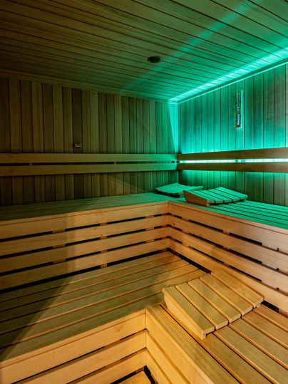 Eine moderne Sauna mit Holzbank und sanfter Beleuchtung. Die Wände sind aus hellem Holz, was eine entspannende Atmosphäre schafft.