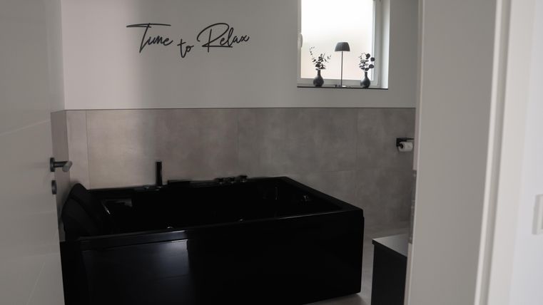 A modern bathroom with a black bathtub. The words “Time to Relax” are written on the wall.
