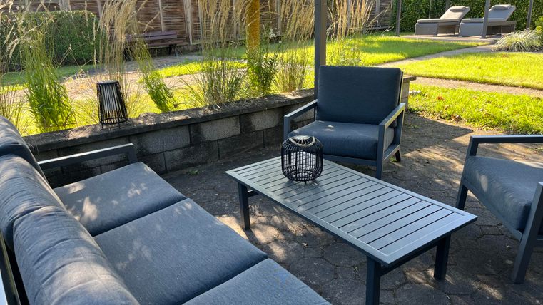 Eine moderne Sitzecke im Freien mit bequemen Sofas und einem Tisch. Umgeben von grünem Gras und Pflanzen bietet sie einen einladenden Ort zum Entspannen.