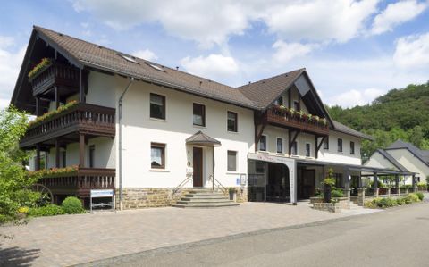 Un bâtiment moderne de plusieurs étages avec des balcons. Il est situé dans un bel environnement avec des arbres et un ciel bleu.