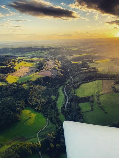 Eine beeindruckende Landschaft mit sanften Hügeln und grünen Feldern im Sonnenuntergang. Der Blick zeigt einen Fluss, der sich durch die Natur zieht.