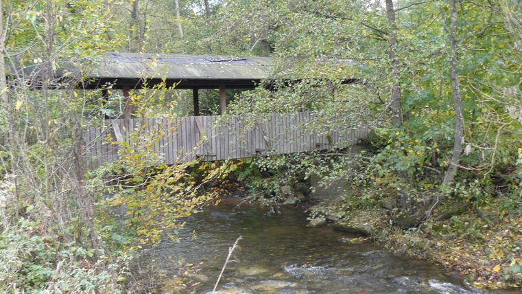 Overdekte houten brug over een rivier in een bosrijk gebied.