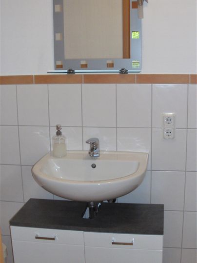 Ein modernes Waschbecken mit einem Spiegel in einem hellen Badezimmer. Die Wände sind gefliest und die Einrichtung ist schlicht und funktional.