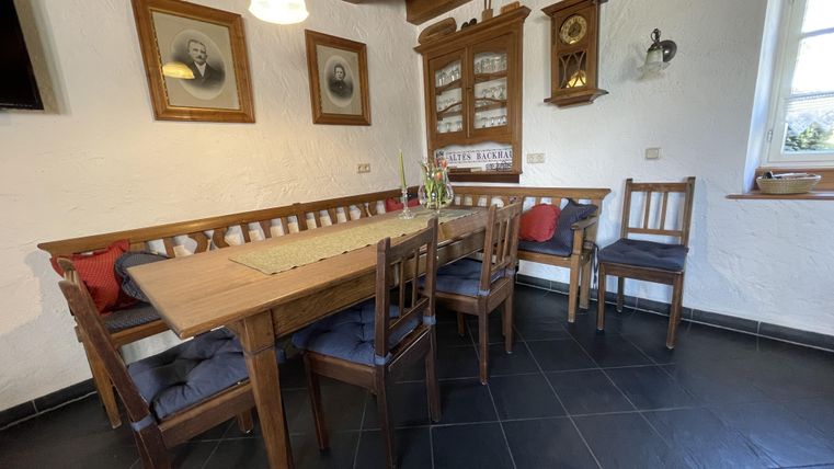 Une salle à manger confortable avec une table en bois et des chaises. Les murs sont décorés avec des images et une horloge, et il y a beaucoup de lumière naturelle.