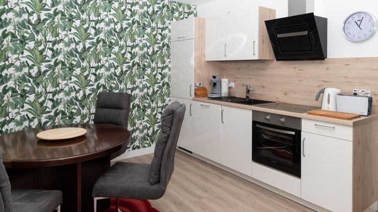 Eine moderne Küche mit einem runden Esstisch und stilvollen Stühlen. Die Wände sind mit einem auffälligen Pflanzenmuster dekoriert.