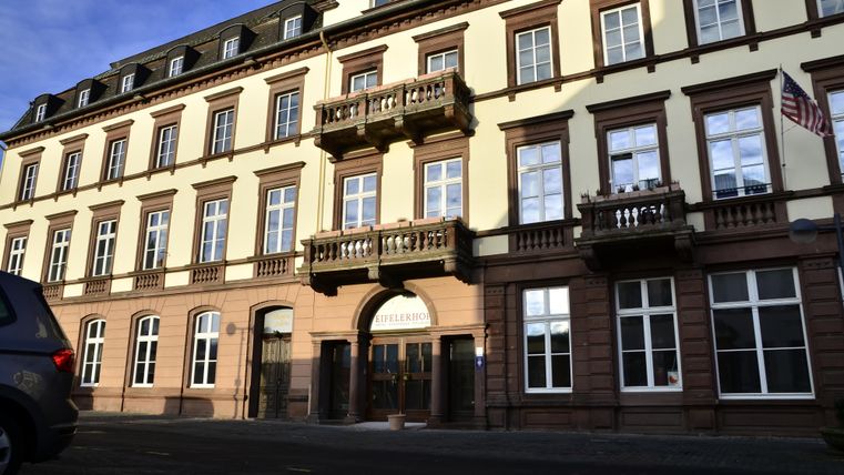 Ein historisches Gebäude mit gelber Fassade und mehreren Fenstern. Es gibt Balkone und einen Eingangsbereich mit einem Rundbogen.