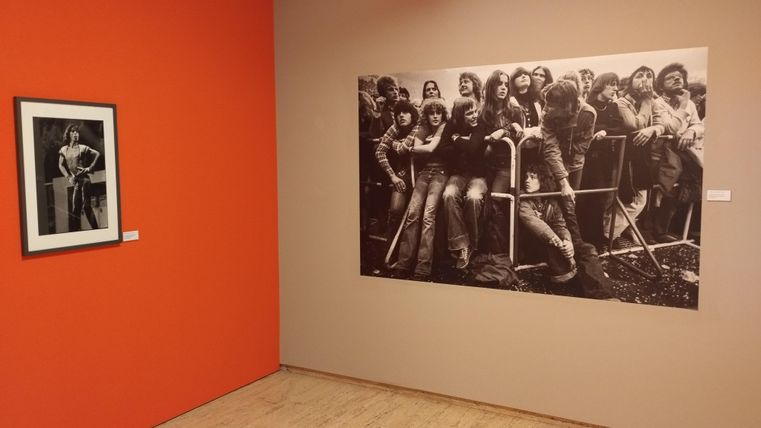 Ein Ausstellungsraum mit zwei Bildern an der Wand. Links ein Schwarz-Weiß-Foto einer Person, rechts ein großes Schwarz-Weiß-Bild mit einer Gruppe junger Menschen.