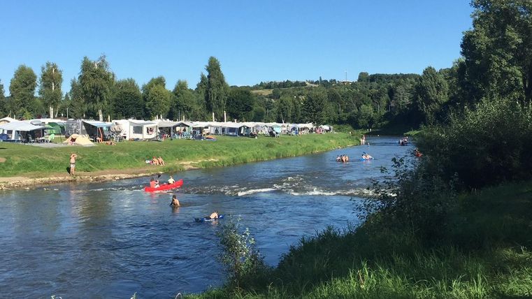 Une belle rivière avec des nageurs et des canoéistes. En arrière-plan, des campings sous un ciel bleu clair sont visibles.