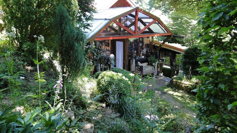Ein charmantes kleines Gartenhaus umgeben von üppigem Grün und bunten Pflanzen. Die Lichtdurchflutung des Hauses schafft eine einladende Atmosphäre.
