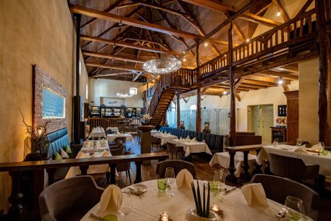 An elegant restaurant with a wooden ceiling and cozy tables. The décor is modern and inviting, with a gallery on the upper floor.