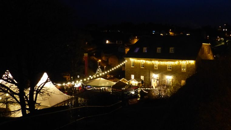 Ein festlich beleuchteter Weihnachtsmarkt in der Dämmerung. Stände und ein Zelt sind schön dekoriert, während die Atmosphäre gemütlich wirkt.