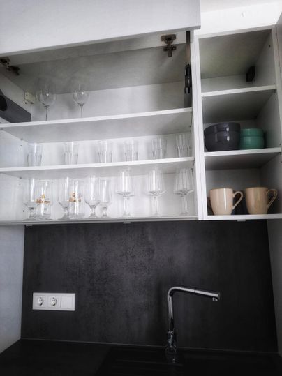 A modern kitchen cabinet with glass dishes and cups. The black kitchen area is well-organized and tidy.