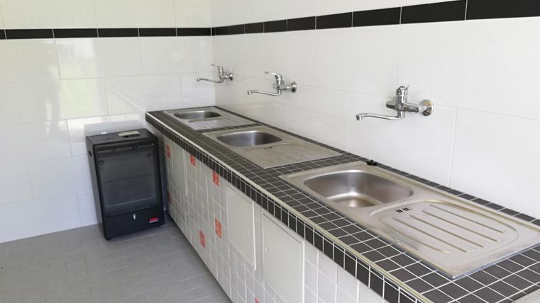 Een moderne keuken met meerdere spoelbakken en een kleine koelkast. De wanden zijn eenvoudig wit betegeld.