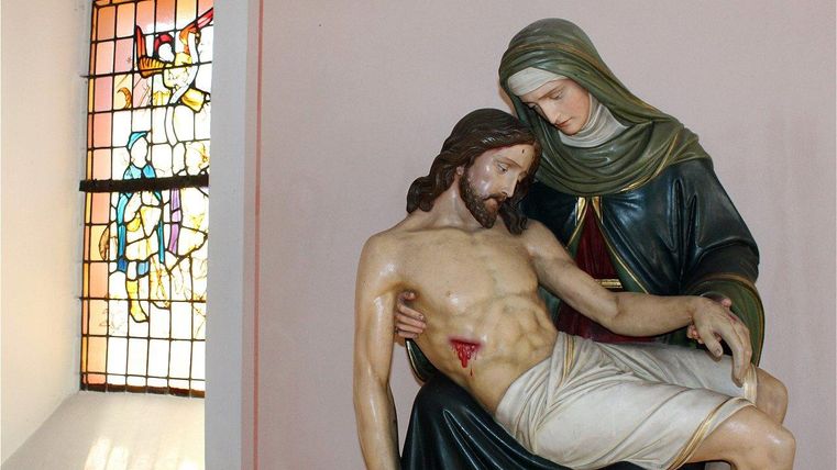 Une statue de Marie tenant le corps de Jésus. En arrière-plan, on peut voir une vitre colorée.