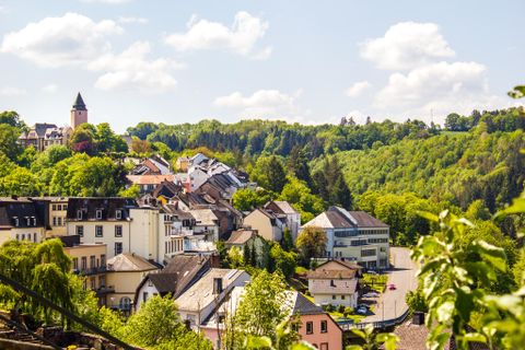 Eine malerische Stadt mit bunten Häusern und sanften Hügeln im Hintergrund. Der Himmel ist klar und die Natur ist grün und einladend.