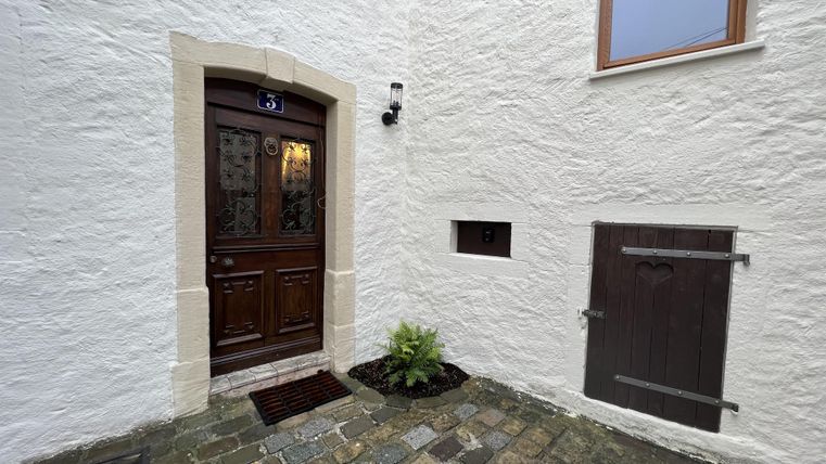 Een mooie ingang met een houten deur en een geplaveide oprit. De muren zijn wit en het raam is goed zichtbaar.