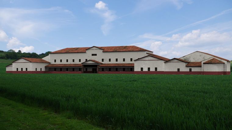 Ein großes, modernes Gebäude mit rotem Dach steht vor einem grünen Feld. Der Himmel ist blau und mit einigen weißen Wolken verziert.