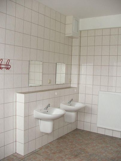 Une salle de bains simple avec deux lavabos et de grands miroirs muraux. Les murs sont carrelés et le sol est revêtu de dalles.