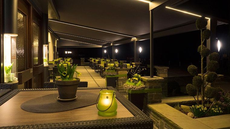 Eine gemütliche Terrasse bei Nacht mit modernen Möbeln und kleinen Pflanzen. Die sanfte Beleuchtung schafft eine entspannte Atmosphäre.