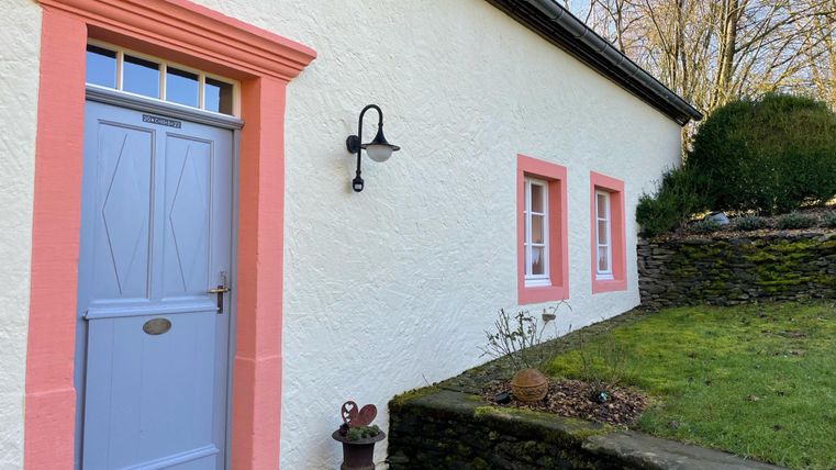 Une maison confortable avec une façade lumineuse et une porte bleue. Devant la maison se trouve un petit jardin avec des pierres et des plantes vertes.