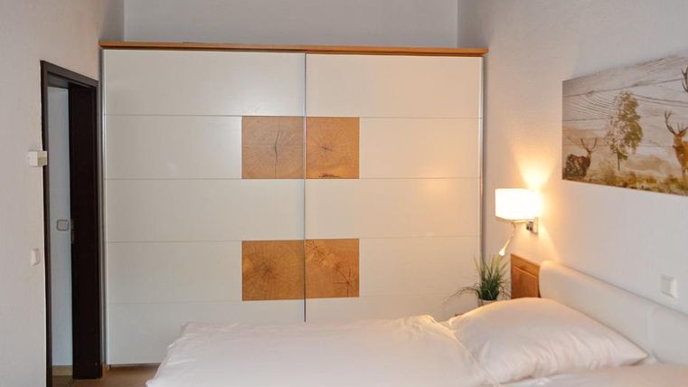 Ein modernes Schlafzimmer mit einem großen weißen Kleiderschrank und einem gemütlichen Bett. An der Wand hängt ein Bild von einer Landschaft.