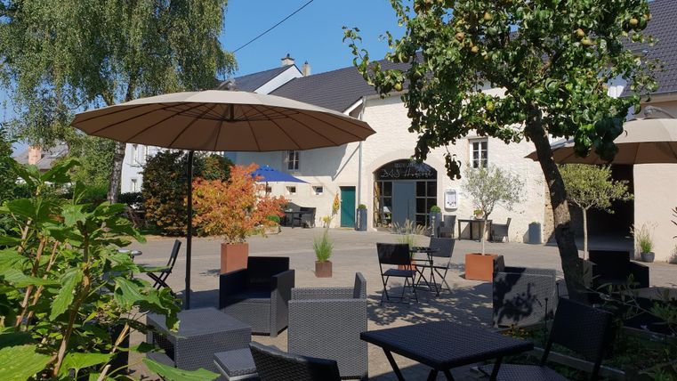 Een gezellige buitenruimte met tafels en stoelen onder een parasol. Omringd door bomen en planten in een uitnodigende ambiance.
