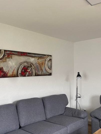 Ein gemütliches Wohnzimmer mit einem grauen Sofa und einem Holztablett. An der Wand hängt ein modernes Kunstwerk.