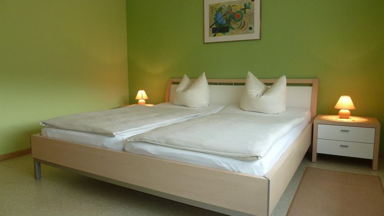 Ein gemütliches Schlafzimmer mit einem großen Bett und zwei Kissen. Die Wände sind in einem freundlichen Grüntton gestrichen, und es gibt sanfte Beleuchtung durch Nachttischlampen.