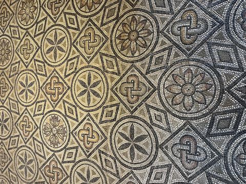 Ein eleganter Mosaikboden mit verschiedenen geometrischen Mustern und floralen Motiven. Die Farben sind in neutralen Tönen gehalten, was dem Design einen klassischen Look verleiht.