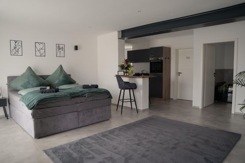 A modern bedroom with a large, comfortable bed and elegant decor. At a small bar, there are chairs, and there is a well-kept, open kitchenette.