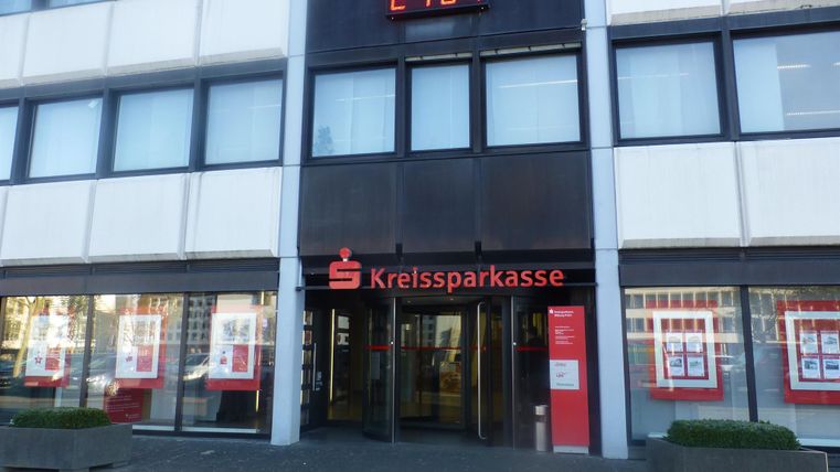 Ein modernes Gebäude mit der Aufschrift "Kreissparkasse". Über dem Eingang zeigt eine digitale Uhr die Zeit an.
