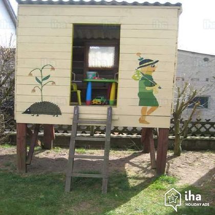 A playhouse on stilts with colorful paintings of a plant and a girl. It stands in a green garden.