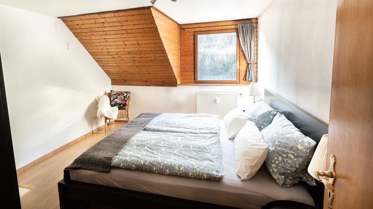 A cozy bedroom with a large bed and light wood decor. A window provides daylight and a view outside.