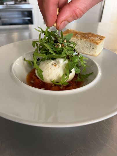 Une assiette avec de la burrata fraîche dans une sauce tomate, garni de feuilles vertes. À côté se trouve un morceau de pain.