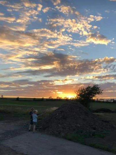 Deux enfants se tiennent devant une colline de terre et observent le coucher de soleil. Le ciel est rempli de nuages colorés et de teintes chaudes.