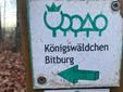 Schild mit der Aufschrift 'Königswäldchen Bitburg' und einem grünen Pfeil nach links.