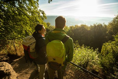 Zwei Wanderer mit Rucksäcken genießen die Aussicht von einem Aussichtspunkt im Wald.