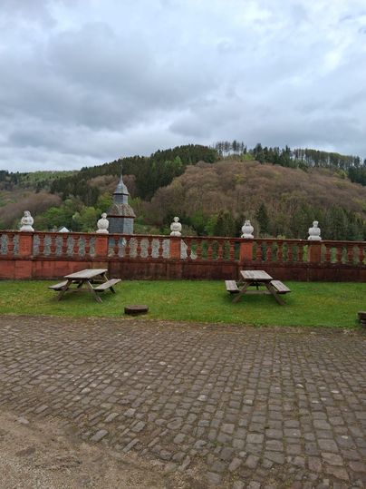 Une vue sur un paysage verdoyant avec des collines douces en arrière-plan. Au premier plan, il y a plusieurs tables en bois sur un sol pavé.