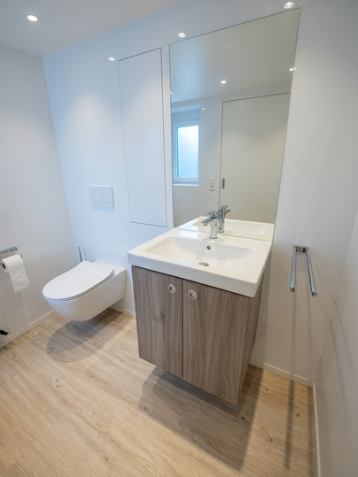 Ein modernes Badezimmer mit einem hellen Waschbecken und Holzschrank. Die Wände sind weiß, und es gibt viel natürliches Licht.