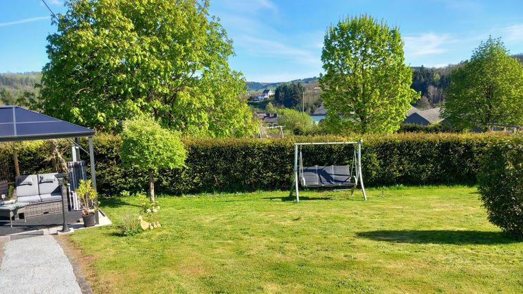 A well-maintained garden with a swing and a beautiful view of the landscape. Green trees and a blue sky create an inviting atmosphere.