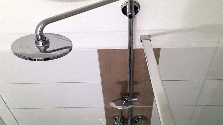 Un pommeau de douche moderne en chrome au plafond. Il est relié à un élégant robinet mural.