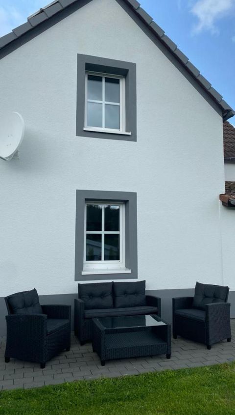 Ein gemütlicher Sitzecke mit schwarzen Möbeln vor einem weißen Haus. Die grüne Wiese und der blaue Himmel schaffen eine einladende Atmosphäre.