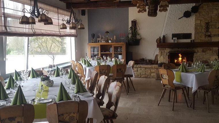 Ein eleganter Speisesaal mit gedeckten Tischen und grünen Servietten. Im Hintergrund ist ein Kamin, der eine gemütliche Atmosphäre schafft.