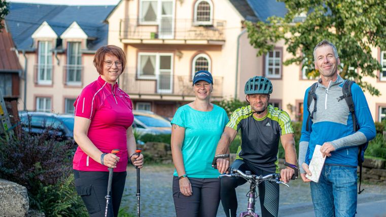 Eine Gruppe von Menschen steht draußen in einer Wohngegend. Sie sind bereit für Outdoor-Aktivitäten wie Wandern und Radfahren.