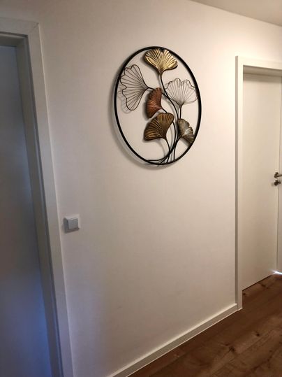 A bright hallway with a round wall decoration made of metallic leaves. On the right is a door leading to another room.