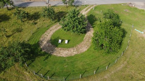 A green meadow with a large round path and several trees. In the middle, there are two benches.