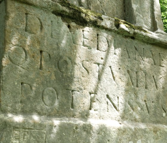 Nahaufnahme einer antiken Inschrift auf einem verwitterten Steinmonument, umgeben von Moos und Wald., &copy; Elke Wagner, Felsenland S&uuml;deifel Tourismus GmbH